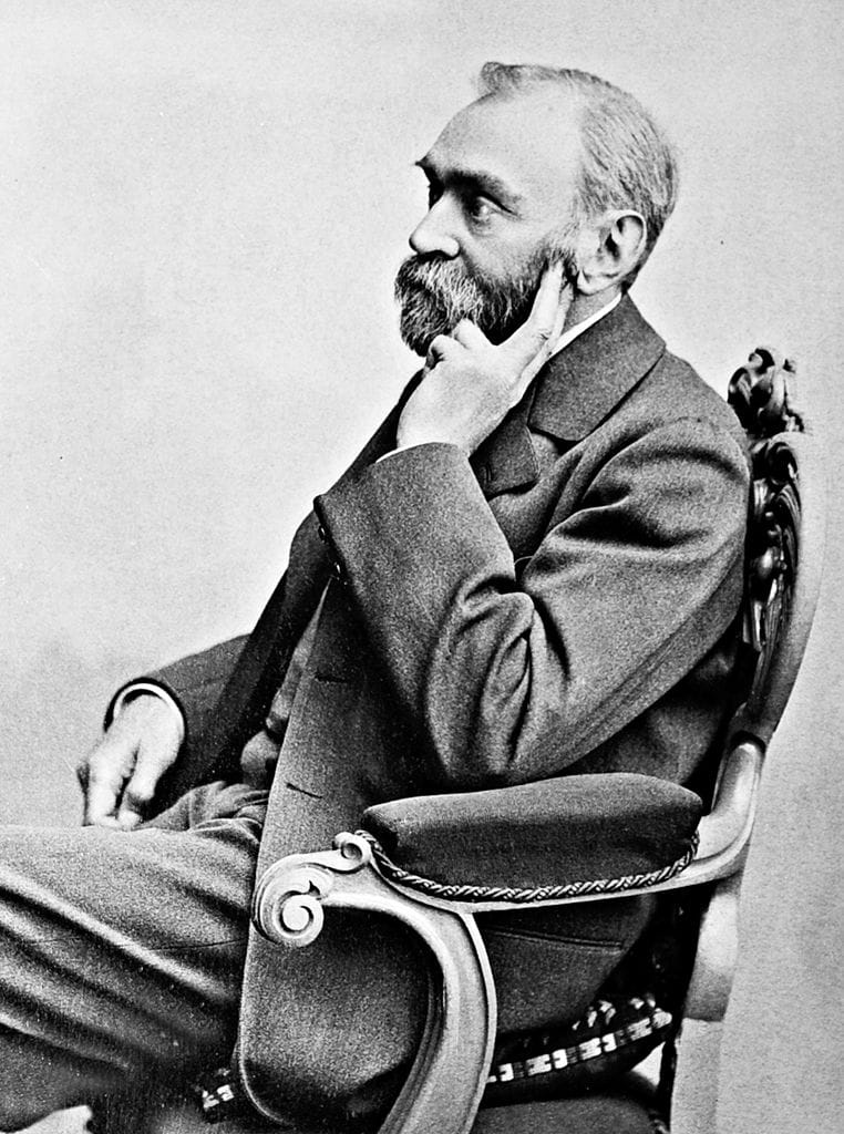 Black-and-white photo of a bearded man in profile, seated in a chair