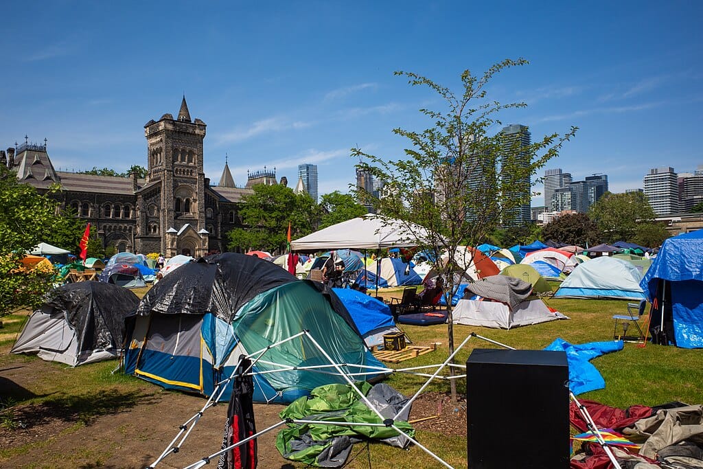 Photo of tents pitched on a lawn in front of a Gothic Revival building; modern buildings are in the background