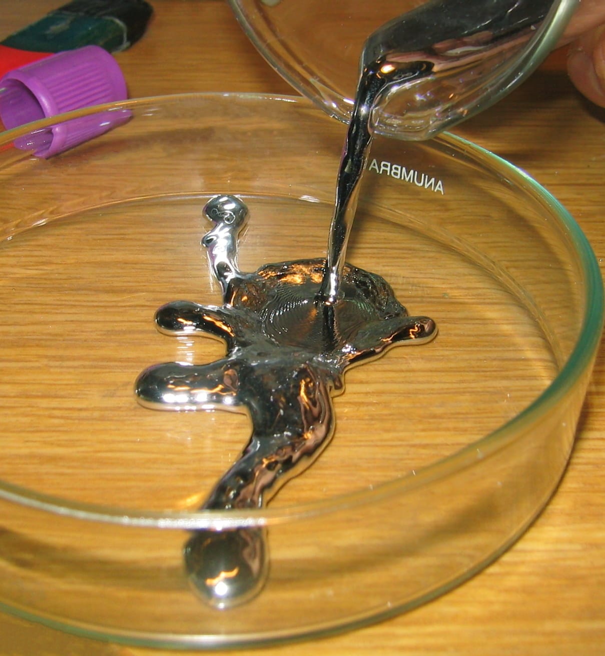 Photo of silvery, metallic liquid being poured from a beaker into a petri dish