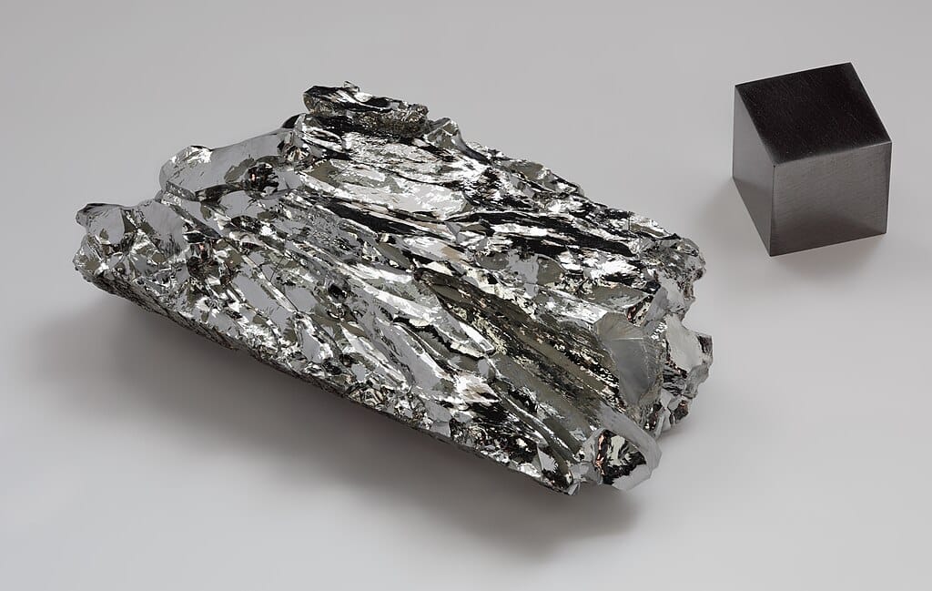 A crystal of silvery metal next to a gray cube