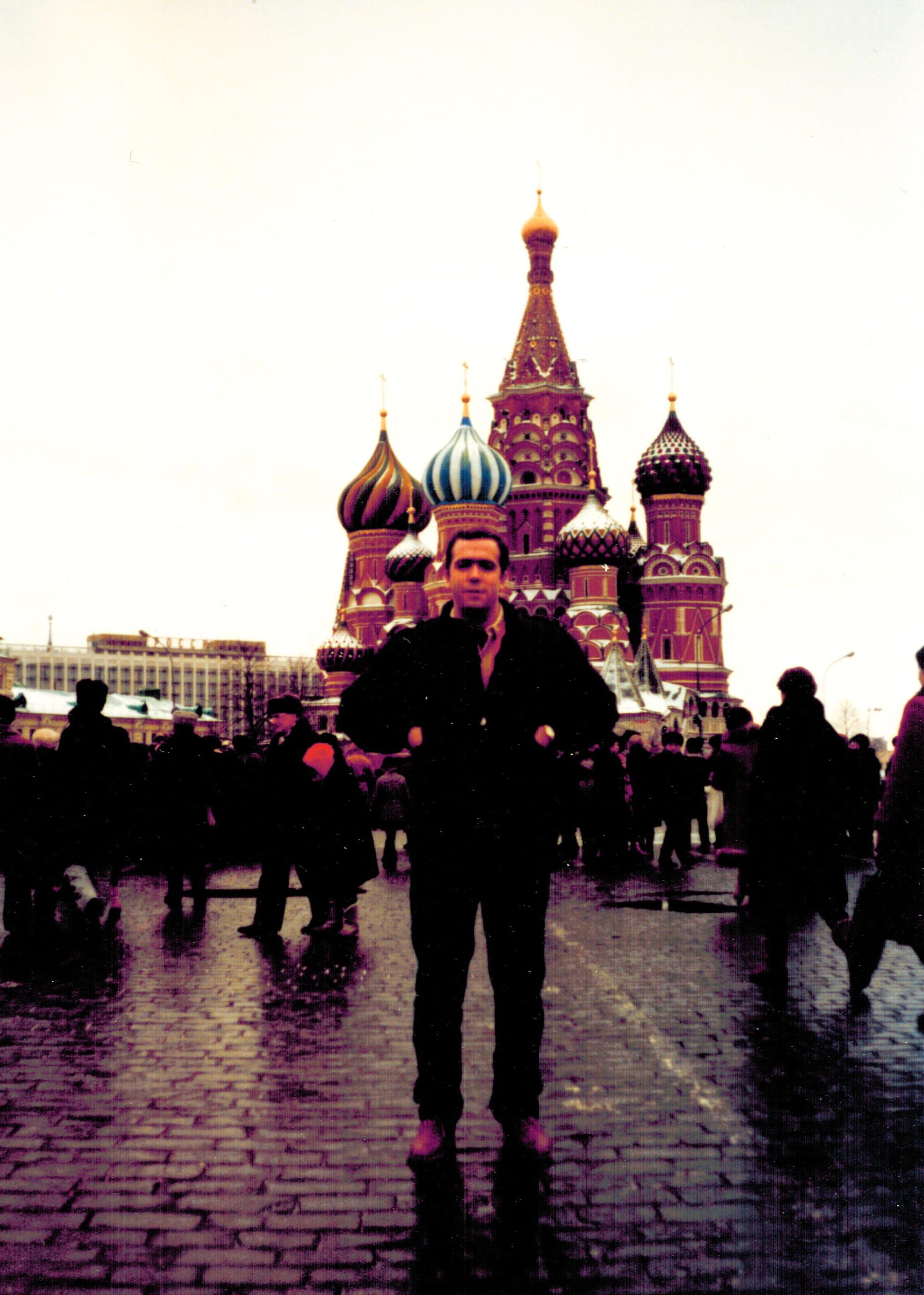 A young man standing in front of an onion-domed cathedral (St. Basil’s Cathedral, Moscow); a crowd is milling about