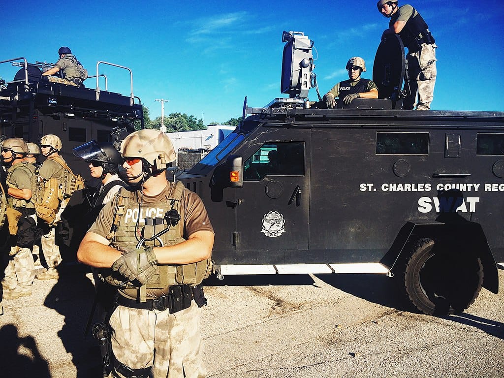 Photo of police in camouflage uniforms and helmets standing near two armored vehicles
