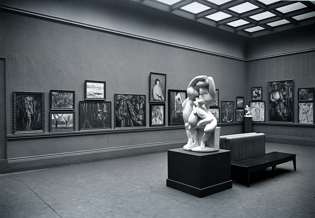 Black-and-white photo of a museum gallery with modern art paintings on the walls and a sculpture in the middle of the room