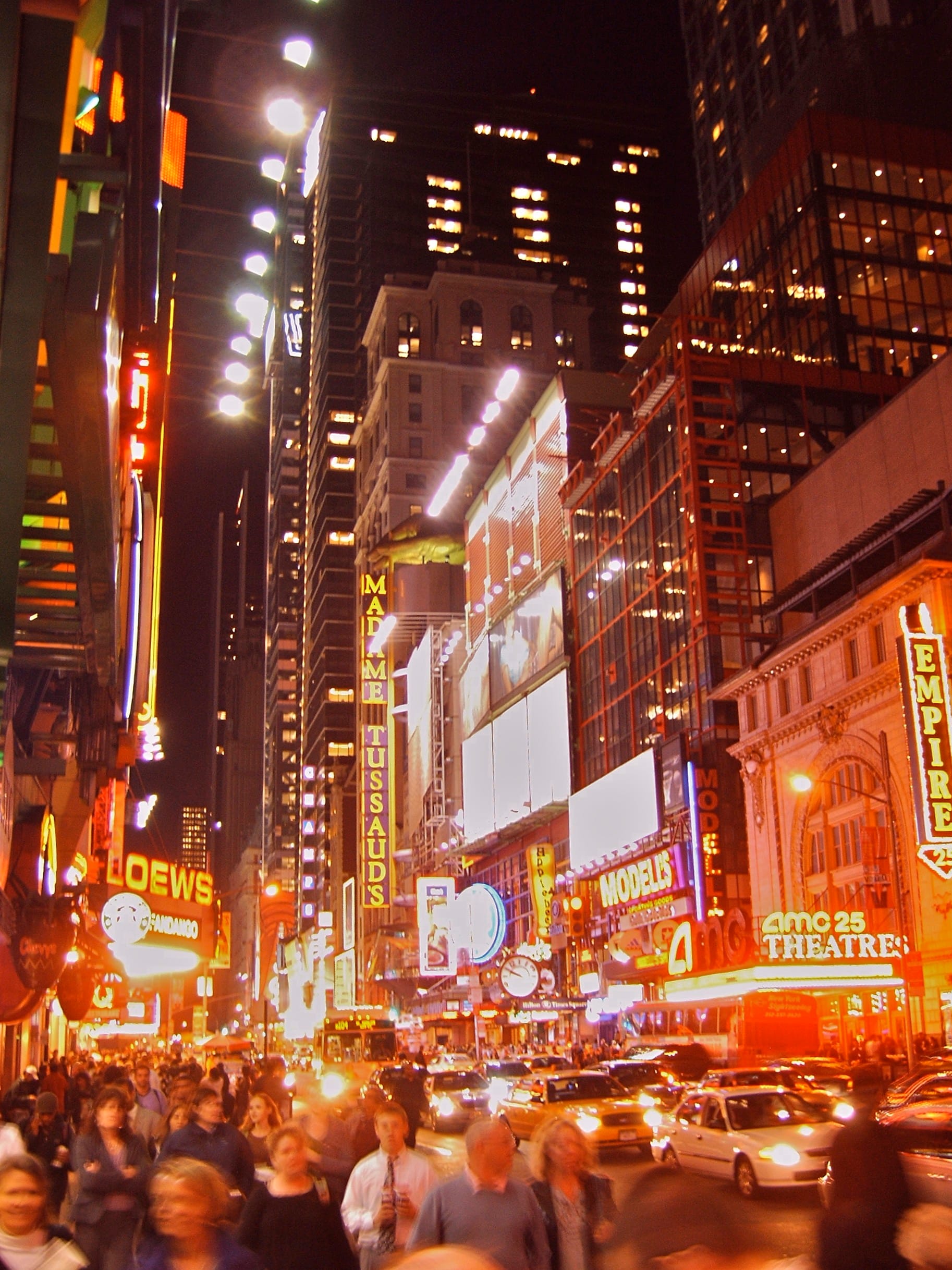 Photo of a busy city street at night, brightly lit by neon and other lights