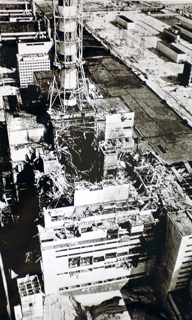 Black-and-white photo of a large industrial building with a caved-in roof and debris strewn about it