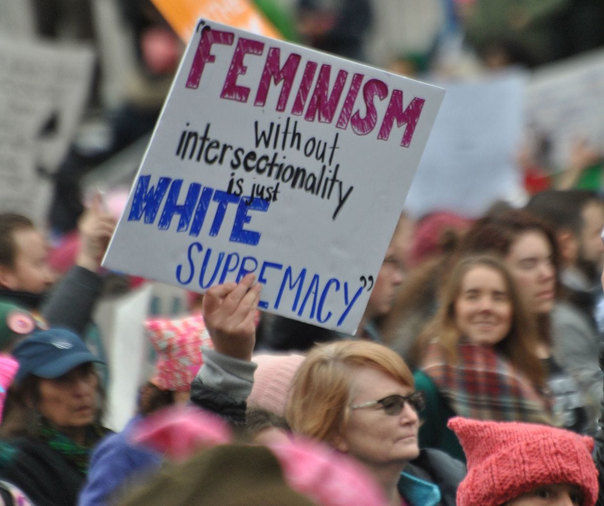 Photo of a crowd of protesters; one is holding a sign reading, “Feminism without intersectionality is just white supremacy"