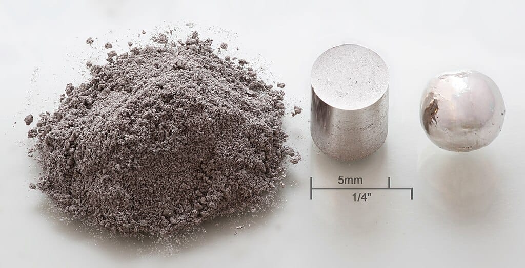 Photo of three samples of a silvery-white metal, a powder, a pressed cylinder, and a round globule