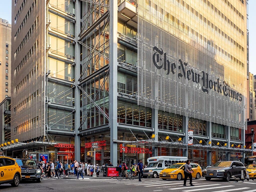 Photo of a busy Manhattan intersection with a large building with a sign reading “The New York Times” in the background