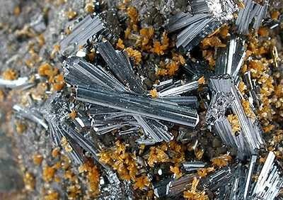 Photo of silver-colored, crystalline rods among dirt particles