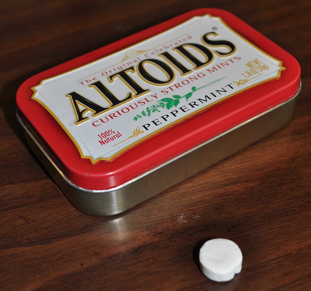 Photo of a container of Altoid peppermints with one mint lying outside the tin