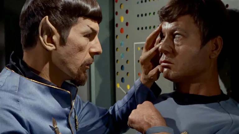 Leonard Nimoy, dressed as Mr. Spock with moustache and goatee, placing his hand on the face of DeForest Kelley/Dr. McCoy