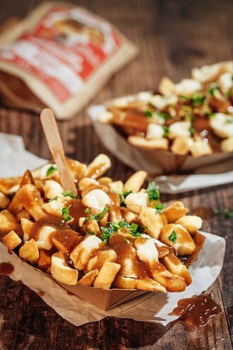 A photo of poutine (French fires, cheese curds, and gravy) served in a cardboard carton