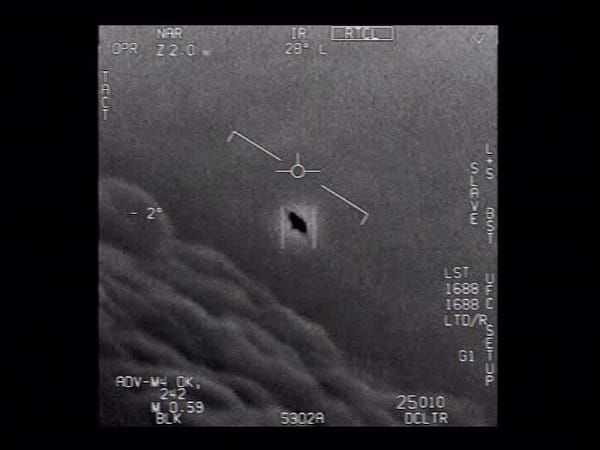 B&W photo of a dark, saucer-shaped object with a light glare or aura surrounding it above a layer of clouds