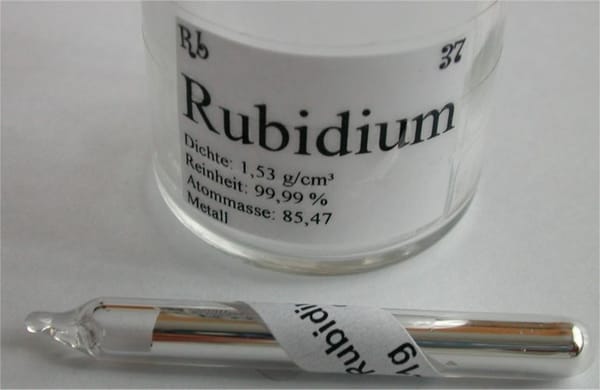 A glass ampule containing a silvery metal with a label detailing the sample’s properties