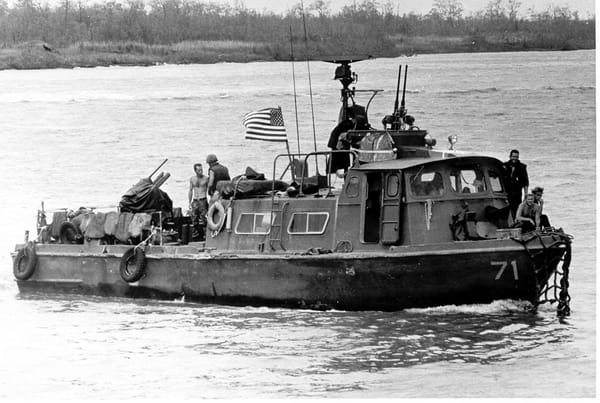 Black-and-white photo of a river craft, flying the American flag and armed with machine guns