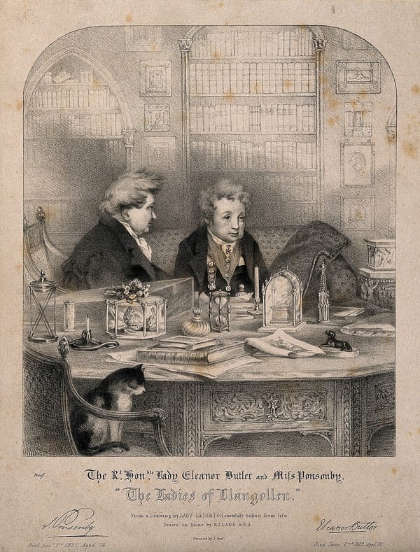 Two women in 19th-century men’s attire sitting in a library