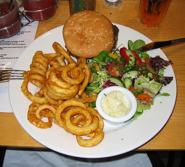 Photo of a plate containing a hamburger, curly fries, and salad