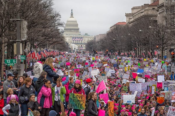 Photograph of a crowd of mostly women bearing protest signs filling Pennsylvania Avenue in front of the US Capitol