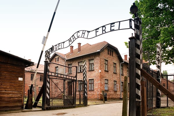 An open gate with the words “Arbeit Macht Frei” (Work sets you free) over the top; a brick building is behind it