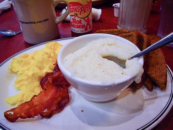 Photo of a bowl of hominy grits beside servings of scrambled eggs, bacon, and toast