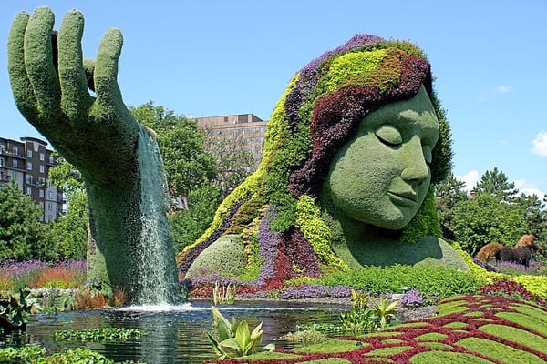Photo of a giant floral sculpture of a woman rising from the earth and sea